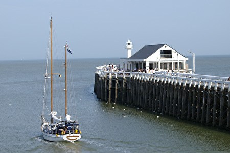 a sailboat passes along the eastern pier with white brasserie